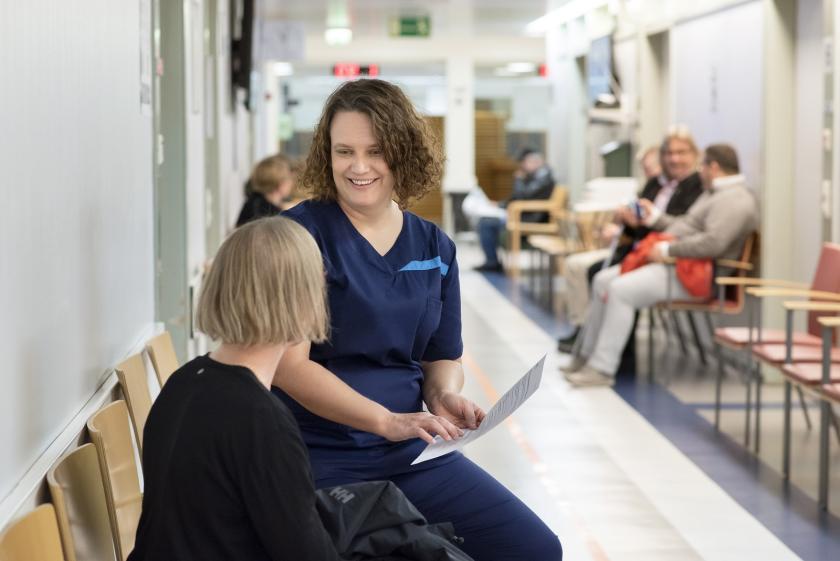 Hoitaja juttelee potilaan kanssa sairaalan käytävällä.