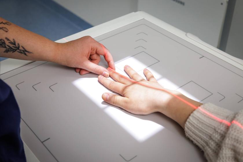 Yksi käsi asettelee toista kättä röntgenkuvauslaitteeseen.