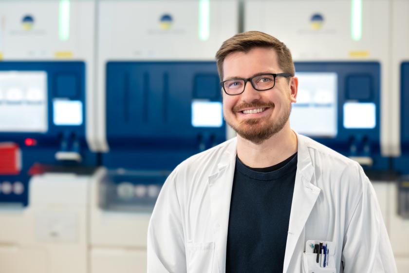 HUSin lääkäri valkoisessa takissa seisoo laboratorion analyysilaitteiden edessä.