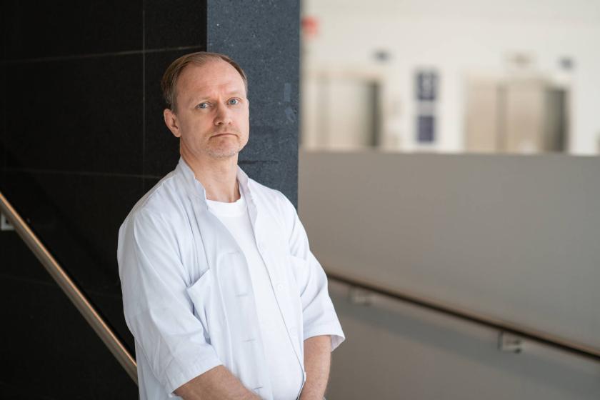 En man i vit skjorta står vid en vägg i en modern byggnadsinteriör.