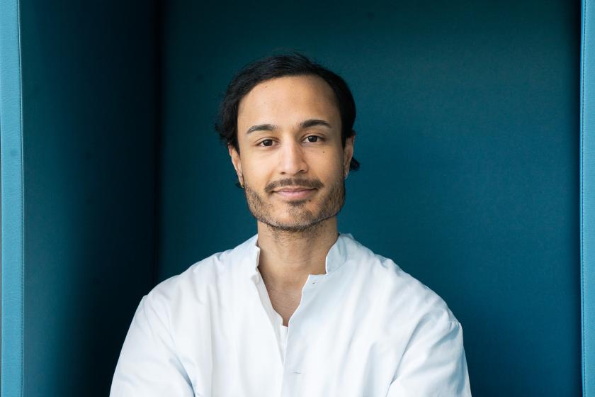 Rahul Raj in a white shirt looking at the camera against a blue background.