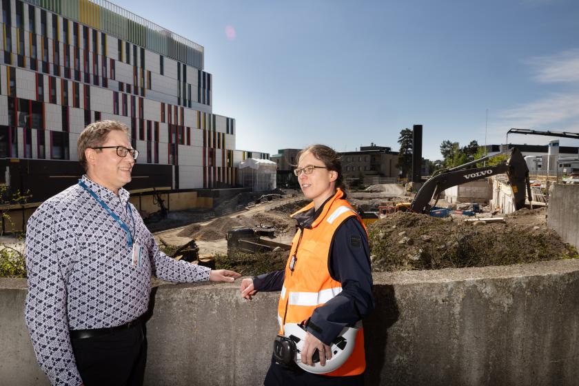 Kaksi henkilöä keskustelee rakennustyömaan edessä Meilahdessa. Toisella heistä on työmaavarusteet yllään.