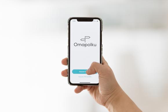 En hand bläddrar på första sidan av Min vårdväg på en mobil.