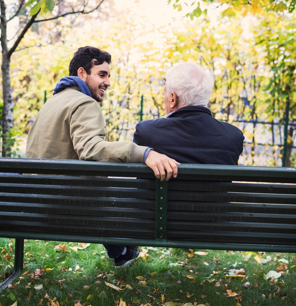En ung och en gammal person som antas vara män sitter på parkbänken med ryggen mot kameran.