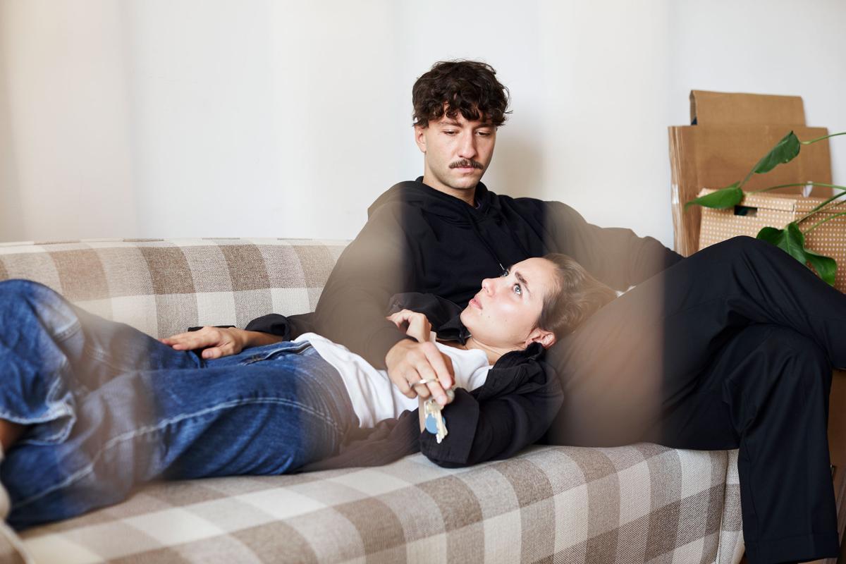 Naisoletettu makaa sohvalla pää miesoletetun sylissä, joka istuu hänen vieressään sohvalla.