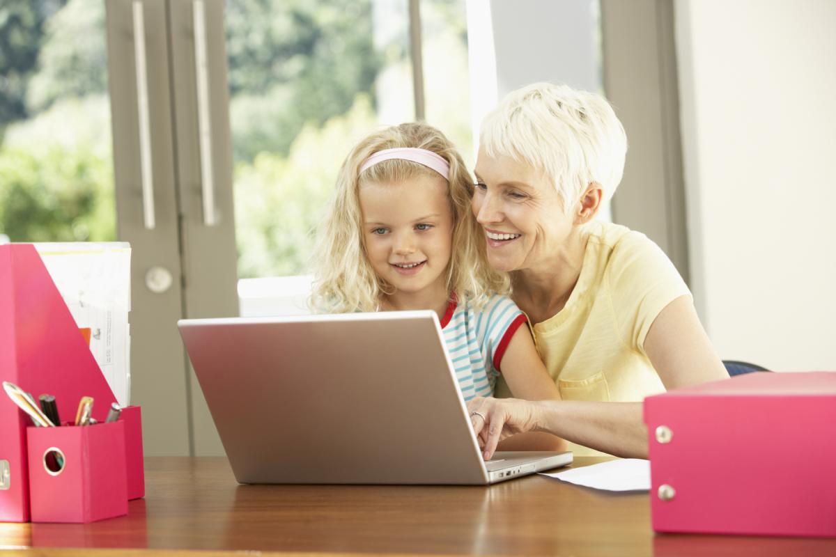 Lapsi ja aikuinen istuvat pöydän ääressä ja tutkivat kannettavaa tietokonetta.