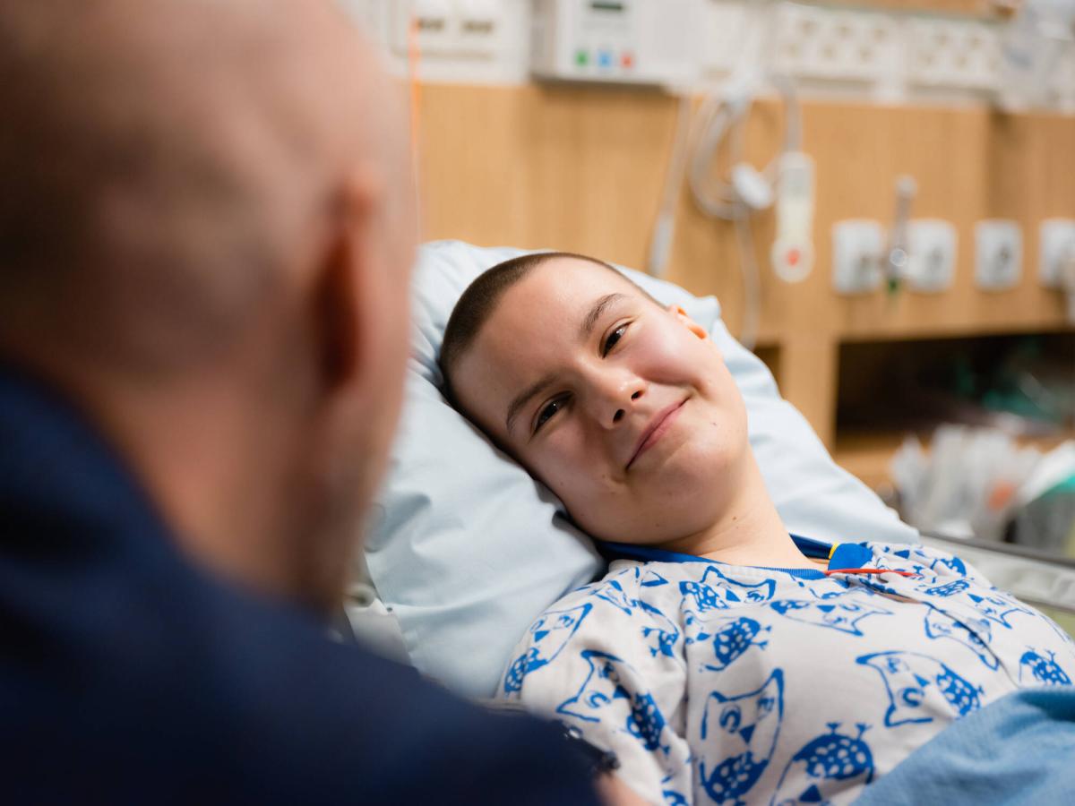 Potilas makaa sairaalasängyssä ja hymyilee läheiselleen.