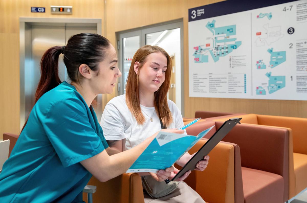 Hoitaja ja toinen henkilö istuvat sairaalan aulassa ja tutustuvat esitteeseen.