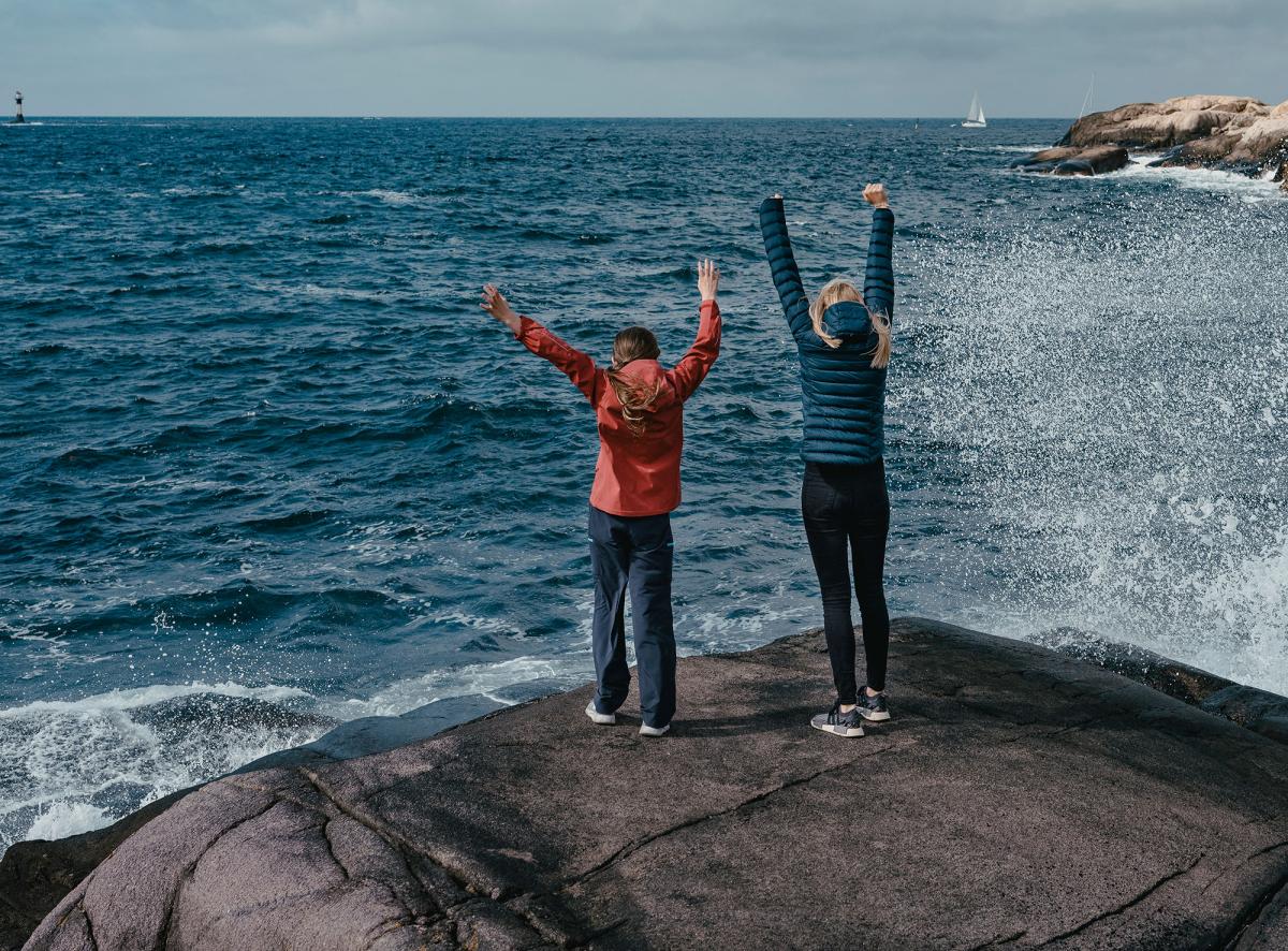 Ett barn och en vuxen med händerna i luften på stranden.