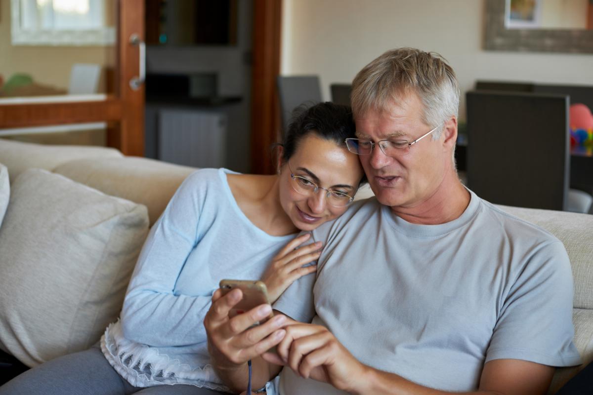 Nais- ja miesoletettu istuvat sohvalla ja katsovat kännykkää.