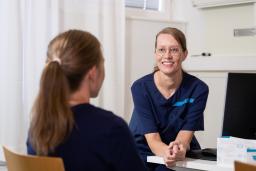 Kätilö Heli Kaukola katsoo hymyillen edessään istuvaa henkilöä.