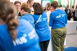 Messutiskillä paljon HUSin henkilökuntaa, yleisöä toisella puolella.