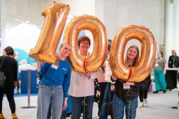 Kolme naista pitelee folioilmapalloja, joista muodostuu luku sata.