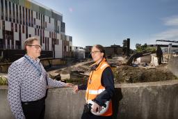 Kaksi henkilöä keskustelee rakennustyömaan edessä Meilahdessa. Toisella heistä on työmaavarusteet yllään.